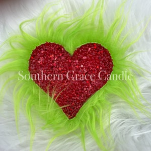 May include: A red glitter heart surrounded by green fuzzy trim.  Southern Grace Candle is written in white text on the heart.