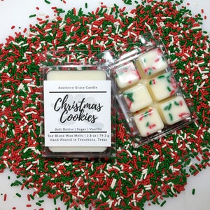 May include: Six white wax melts in a clear plastic container. The wax melts are decorated with red and green sprinkles. The container is surrounded by red, green, and white sprinkles. The label on the container reads "Southern Grace Candle Christmas Cookies Soft Butter | Sugar | Vanilla Soy Blend Wax Melts 2.8 oz | 79.3 g Hand-Poured in Texarkana, Texas".