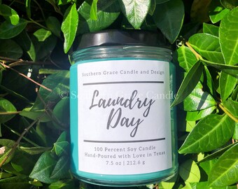 May include: A teal blue soy candle with a white label that reads "Laundry Day". The label also states "100 Percent Soy Candle", "Hand-Poured with Love in Texas", and "7.5 oz | 212.6 g".