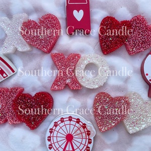 May include: A collection of Valentine's Day themed decorations, including a red and white heart, a white letter X, a red letter O, a red and white heart, a red and white rainbow, a red and white gumball machine, and a red and white Ferris wheel. The decorations are all covered in glitter.