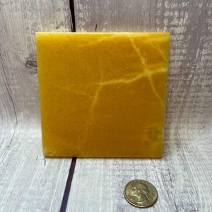 May include: A square yellow onyx coaster with white veining. The coaster is about the size of a quarter.