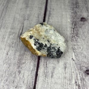 May include: A rough, white and black crystal with a brown, earthy base. The crystal has a natural, raw look and is a great example of a natural mineral.