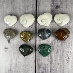 May include: Ten heart-shaped polished stones in various colors and patterns. The stones are arranged in three rows on a light wood background. The stones include white, gray, brown, green, and red.
