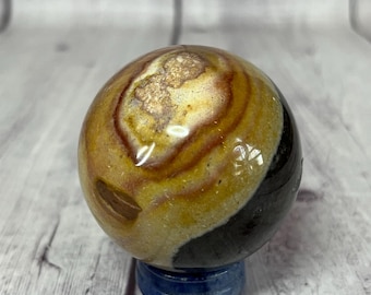 May include: A polished, multi-colored sphere with swirling patterns of brown, yellow, and black. The sphere is sitting on a blue stand.