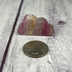 May include: A pink and white cloud-shaped crystal with yellow and orange streaks. The crystal is about the size of a US quarter.