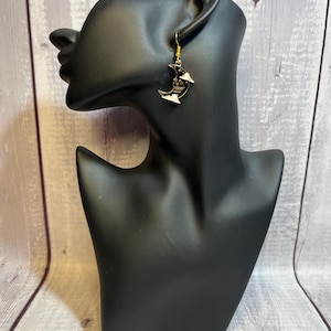May include: A pair of gold-colored earrings featuring a black crescent moon design with a skull face and white cloud accents. The earrings are displayed on a black mannequin head.
