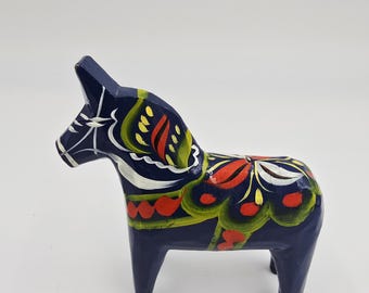 May include: A navy blue wooden Dala horse, a traditional Swedish folk art figurine. It features hand-painted floral patterns in red, yellow, and white. The horse stands on four legs and is a decorative item.