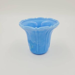 May include: A light blue glass vase with a scalloped rim and a fluted design. The vase is made of opaque glass and has a slightly cloudy appearance.