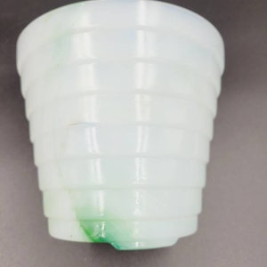 May include: A white and green glass cup with a ribbed design. The cup is opaque and has a swirl of green glass.