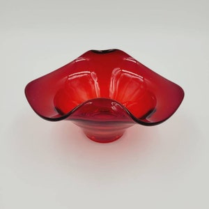 May include: A red glass bowl with a wavy, ruffled edge. The bowl is made of clear glass with a red tint.
