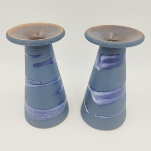 May include: Two blue ceramic candle holders with white and purple glaze. The holders are cone-shaped with a wide, flat top.