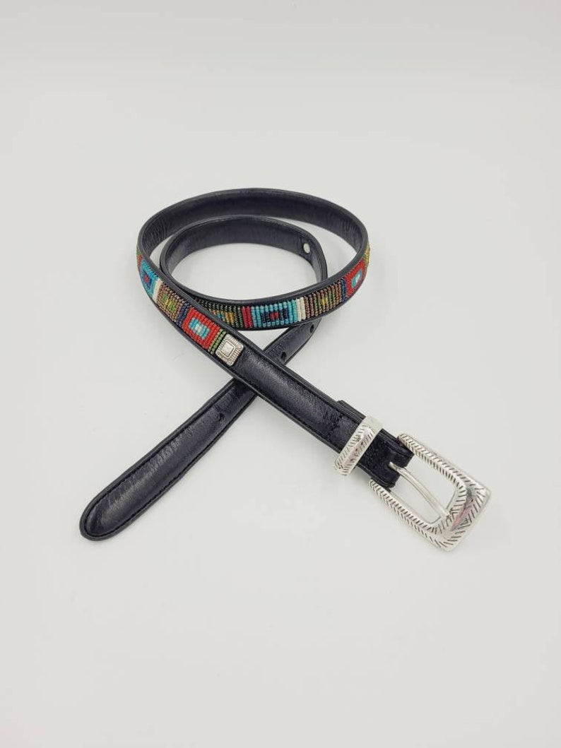 May include: A black leather belt with a silver buckle and colorful beaded design. The beads are arranged in a geometric pattern.
