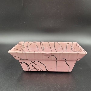 May include: A pink ceramic planter with black abstract lines. The planter has a fluted rim and is rectangular in shape.
