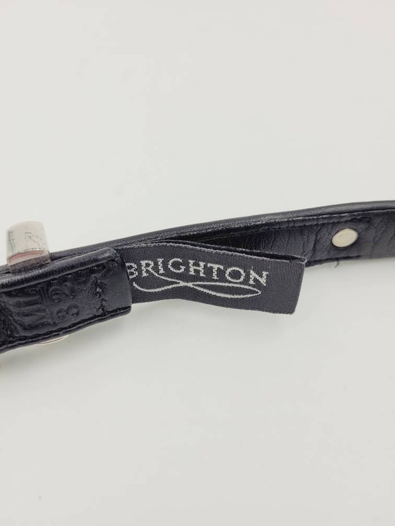 May include: Close-up of a black leather belt with a silver buckle and a black label that reads "BRIGHTON".