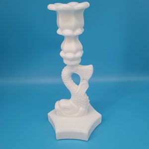 May include: White ceramic candlestick featuring a fish design. The candlestick has a flower-shaped top and a six-pointed star base.