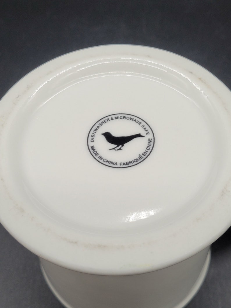 May include: White ceramic mug with a black bird logo that reads "Dishwasher & Microwave Safe. Made in China. Fabrique en Chine."