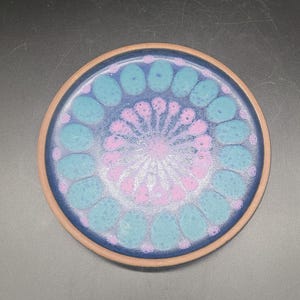 May include: A blue ceramic plate with a pink and blue floral design. The plate has a raised rim and a smooth surface.