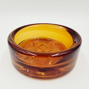 May include: A round amber glass ashtray with a geometric pattern on the bottom.