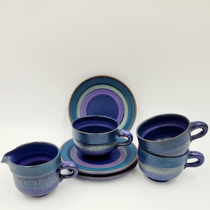 May include: A set of blue and purple ceramic teacups and saucers. The cups have a textured, speckled finish and the saucers have a concentric circle design.