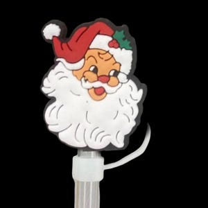 以下が含まれることがあります： サンタクロースの顔が描かれた白いプラスチック製のクリスマスツリーの飾り。サンタは赤い帽子、白いひげ、茶色の顔をしています。