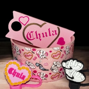 以下が含まれることがあります： ピンクと白のハート型の容器に「Chula」という文字が印刷されています。容器は、ハート、スニーカー、サングラス、そして「Chula」という文字のパターンで飾られています。「Chula」という文字が印刷されたピンクと白のハート型のキーホルダーが2つと、白いスニーカーのデザインが施された黒いキーホルダーがあります。