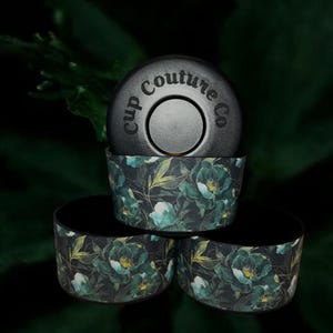 May include: Three black and green reusable cup lids with a floral pattern. The top lid has the text "Cup Couture Co." printed on it.