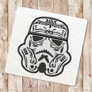 May include: Black and white embroidered design of a Star Wars Stormtrooper helmet with intricate floral patterns.