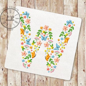 Puede incluir: Un fondo blanco con una gran letra W formada por flores, mariposas y hojas bordadas de colores.