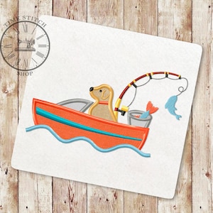 Pode incluir: Um desenho bordado de um cão amarelo num barco vermelho com uma vara de pesca e um peixe azul. O barco está em ondas azuis.
