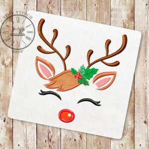 May include: Embroidered design of a reindeer face with brown antlers, a red nose, pink ears, and a green holly wreath with red berries.