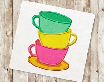May include: A stack of three colourful teacups, with a green cup on top, a yellow cup in the middle, and a pink cup on the bottom. The cups are stacked on a yellow saucer.