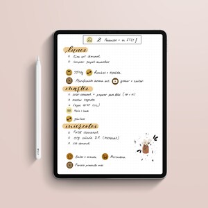 May include: A digital tablet displaying a weekly planner with handwritten notes in Spanish. The planner includes daily tasks, weight tracking, and social media reminders. A white stylus rests beside the tablet on a pink surface. Text on the tablet reads "2 Productes en ETSY!"
