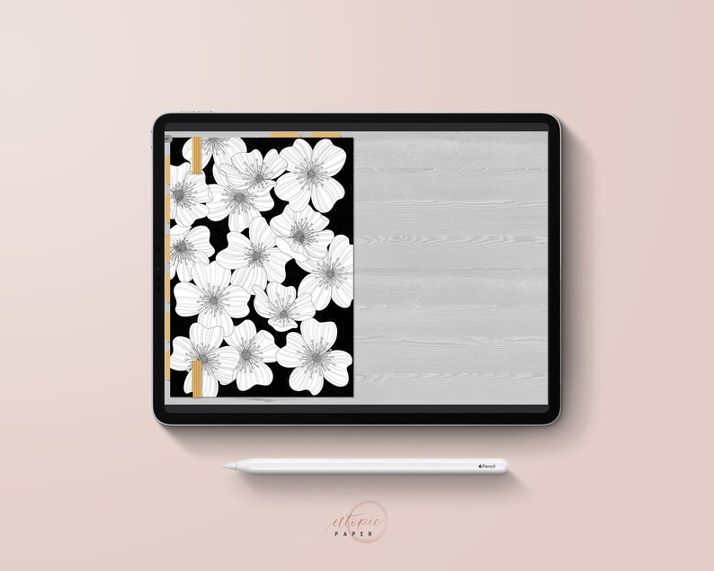 May include: A digital tablet displays a floral design. The design features white flowers on a black background, with a gold border. A white stylus rests below the tablet. The words "utopic paper" are at the bottom.