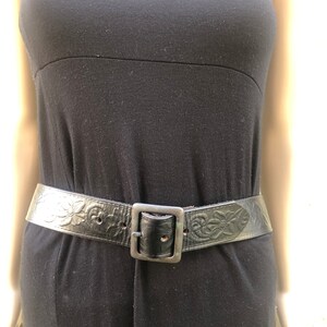 May include: A black leather belt with a floral design and a silver buckle.