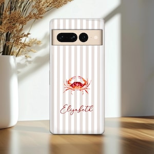 May include: A phone case with a vertical striped pattern in beige and white. A watercolor crab illustration in red and orange is centered on the case, with the name "Elizabeth" in a cursive font below the crab.