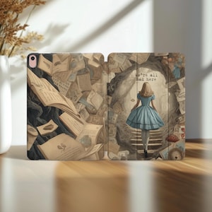 May include: An open tablet case featuring an illustration of Alice in Wonderland. The left side shows a cascade of books and papers. The right side depicts Alice in a blue dress, walking towards a tunnel with the text "we're all mad here."