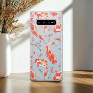 May include: Clear phone case with a pattern of orange and white koi fish and pink cherry blossoms on a light blue background.