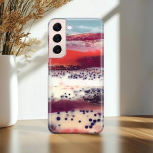 Puede incluir: Una funda para smartphone con un diseño abstracto. La funda presenta capas de tonos rojos, blancos y azules, con pequeños puntos azul oscuro dispersos en la parte inferior. La funda está hecha de un material transparente y brillante.
