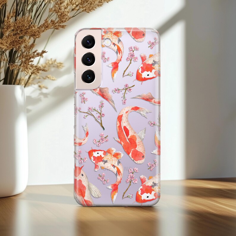 May include: A clear phone case with a design of orange and white koi fish swimming amongst pink cherry blossoms on a light purple background.