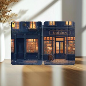 May include: A folding tablet case featuring a dark blue illustration of a bookstore exterior at night. The storefront has large windows displaying shelves of books, warm interior lighting, and a sign above the door that reads Book Store.