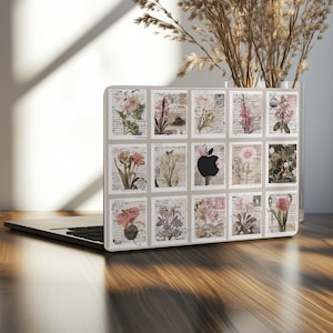 Peut inclure: Un ordinateur portable avec un motif de timbre floral. Le motif présente diverses fleurs et des écritures sur un fond beige. Un logo Apple noir est également visible. L'ordinateur portable est sur une surface en bois.