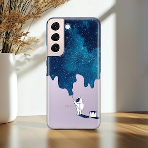 May include: A phone case with a galaxy design and an astronaut painting the galaxy with a paintbrush. The case has a white background and the text "SAMS" is visible at the bottom.