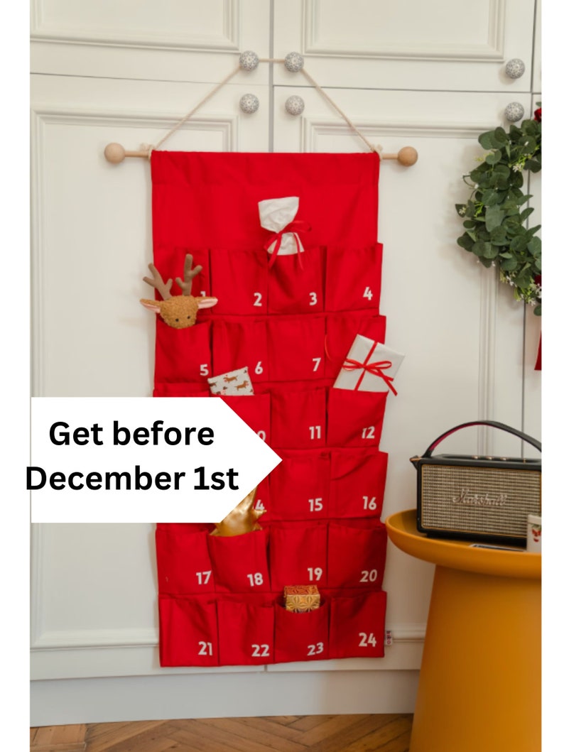 Puede incluir: Un calendario de Adviento de tela roja para colgar en la pared con veinticuatro bolsillos numerados. El calendario presenta n&uacute;meros blancos impresos del 1 al 24, con varios peque&ntilde;os regalos en algunos bolsillos, suspendido de una vara de madera.