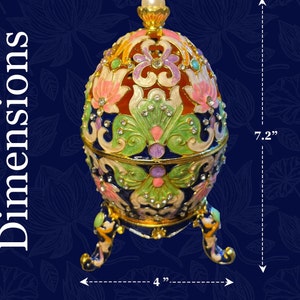 May include: An egg-shaped decorative object with a jewel-toned finish. The egg is 18.3 cm tall and 10.2 cm wide, featuring intricate floral designs in red, green, pink, and blue, with rhinestones and gold trim. It rests on three decorative feet.