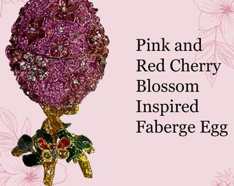 Puede incluir: Un huevo de Fabergé inspirado en las flores de cerezo rosas y rojas. El huevo está adornado con intrincados diseños florales y adornos brillantes. La base es dorada con detalles coloridos.