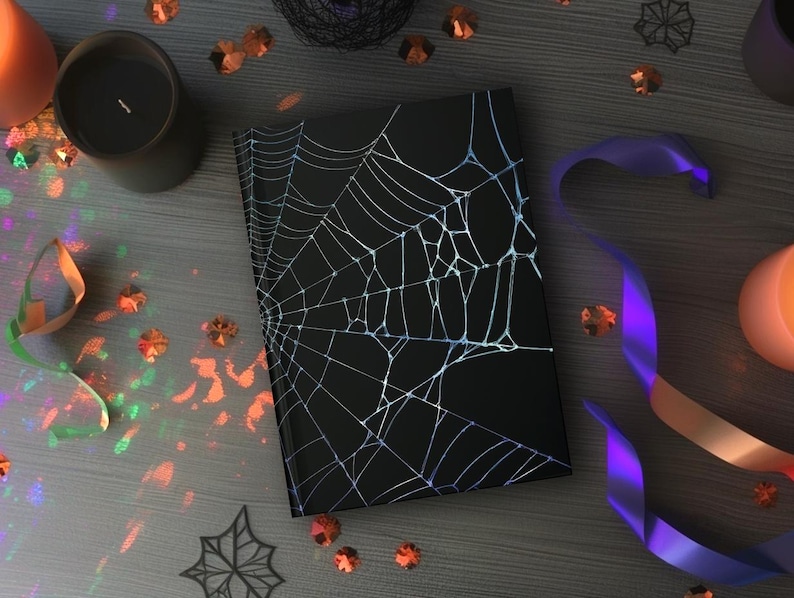May include: A black notebook with a white spiderweb design, surrounded by Halloween decorations. The scene includes candles, confetti, and a purple and orange ribbon, creating a spooky aesthetic.