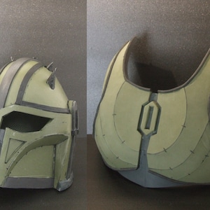 May include: A green and black helmet and chest piece for a costume. The helmet has a black visor and a black stripe design. The chest piece has a black strap and a black design.