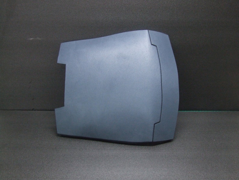 Puede incluir: Una pieza de pl&aacute;stico azul oscuro moldeada con una forma curva y un dise&ntilde;o texturizado en relieve. La pieza tiene un acabado liso y mate.