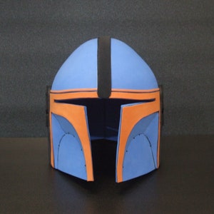 Op de afbeelding: Een blauwe en oranje helm met een zwarte streep in het midden. De helm is gemaakt van schuim en heeft een afgeronde vorm.