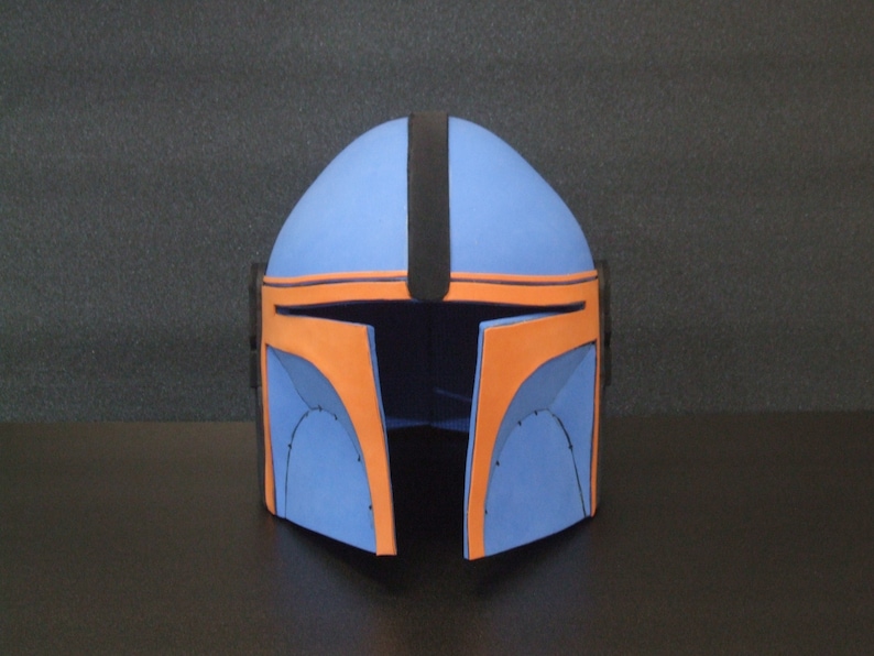 Op de afbeelding: Een blauwe en oranje helm met een zwarte streep in het midden. De helm is gemaakt van schuim en heeft een afgeronde vorm.